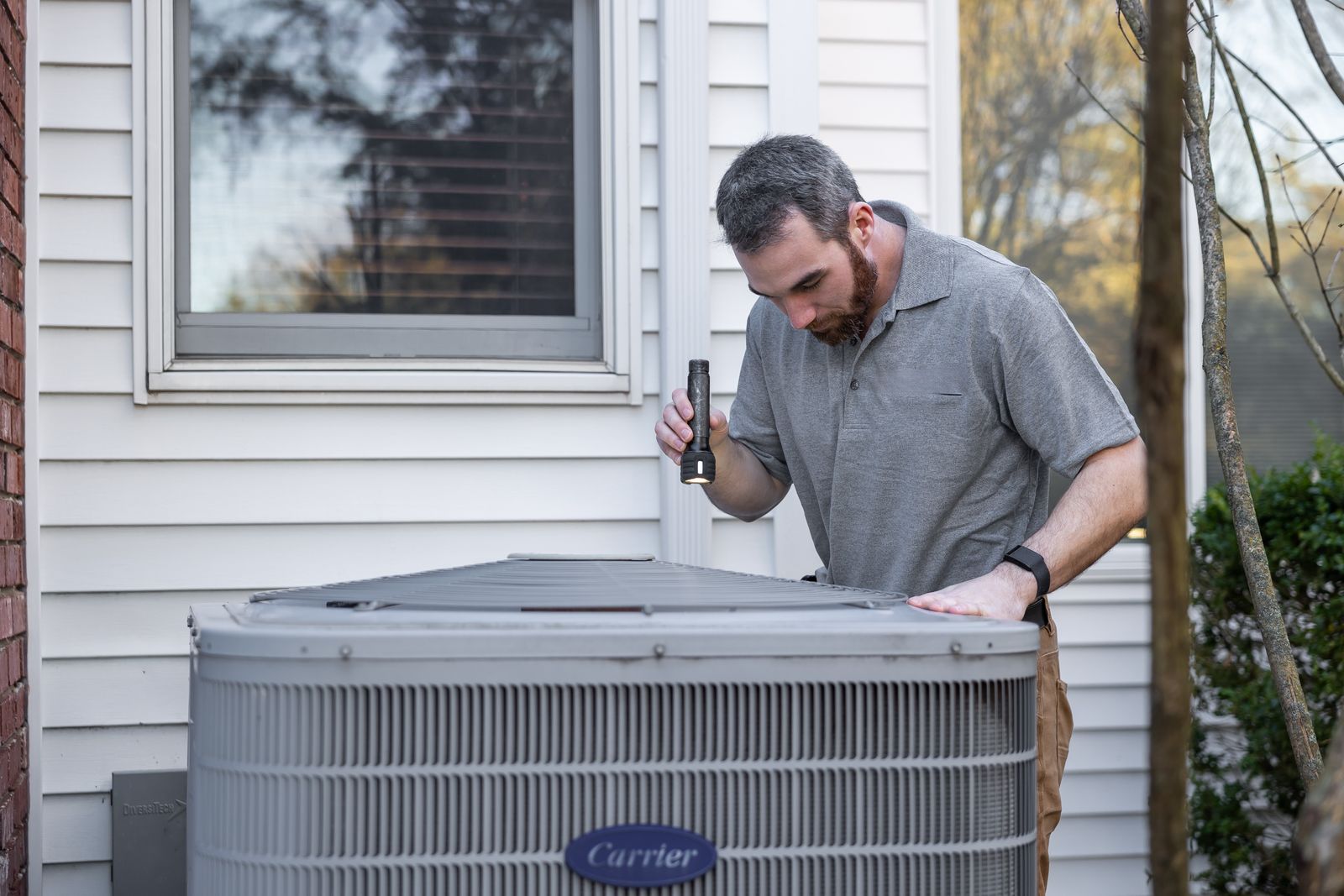 A technician checking an outdoor air conditioning unit beside a house