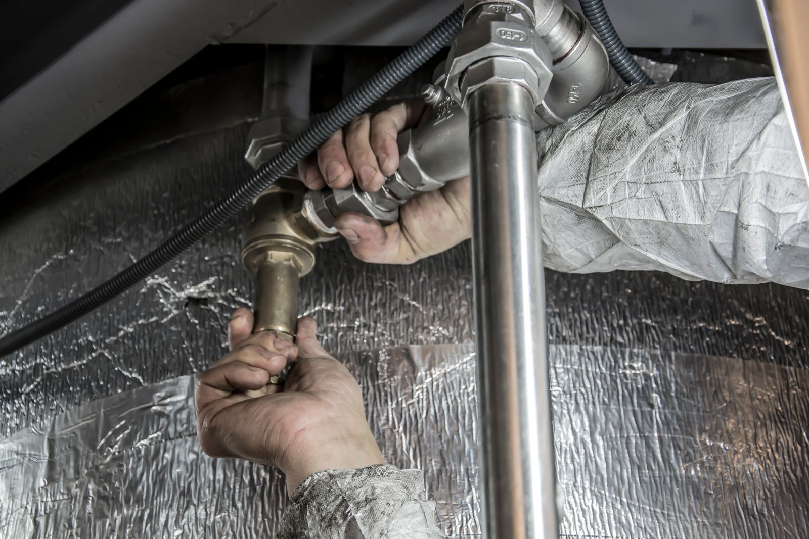 A plumber tightening a pipe fitting under a sink